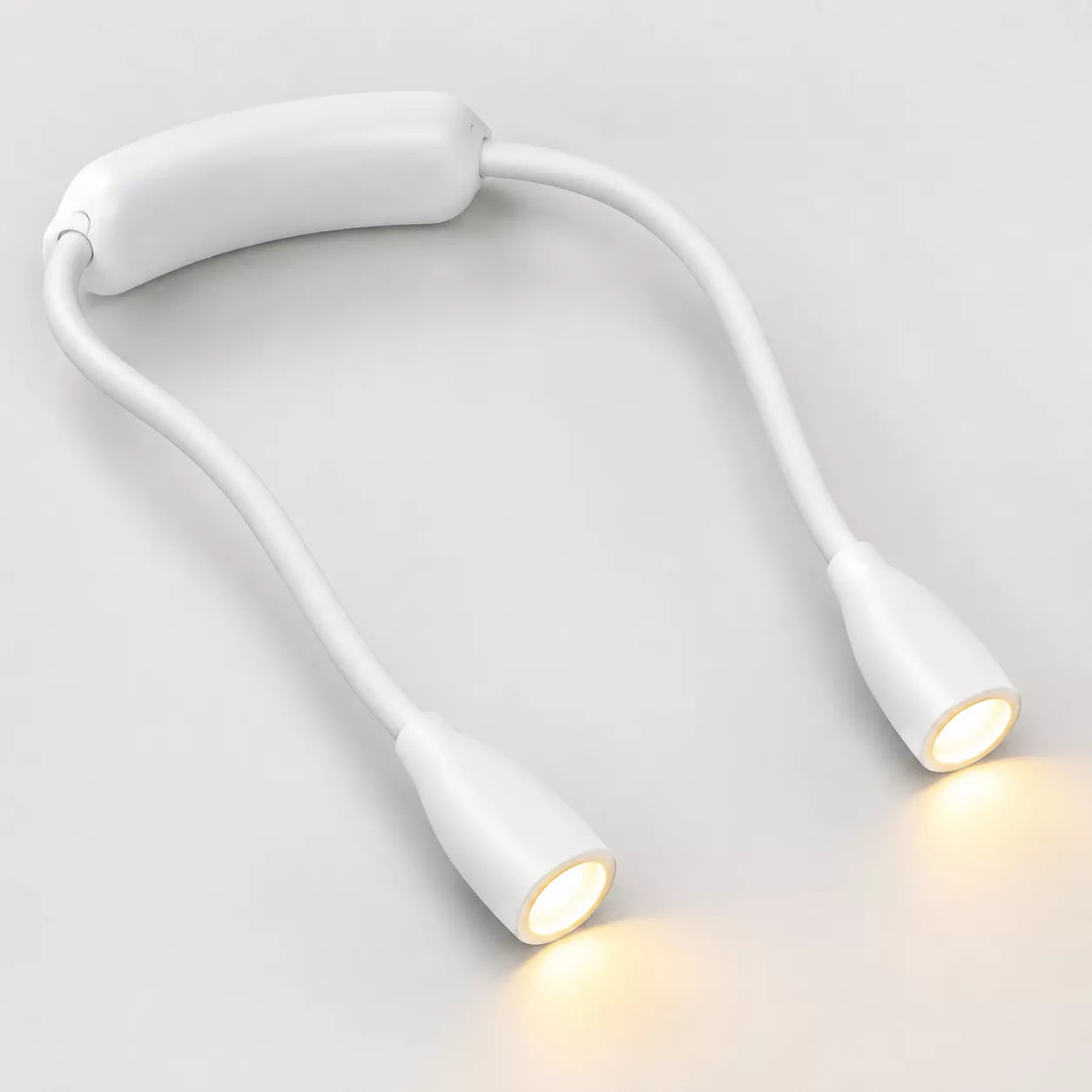 A white dual-head flexible reading light with a padded headband, shown illuminated on a light gray background.